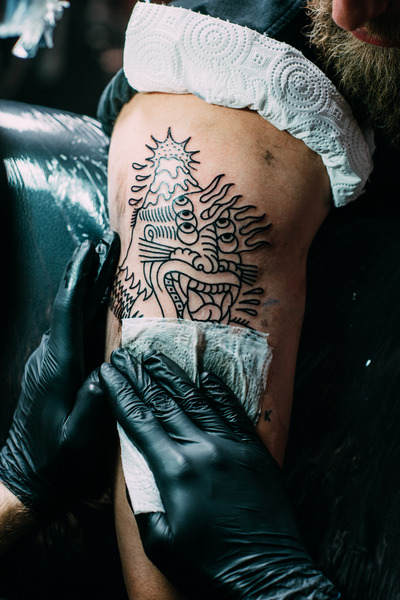 Tätowierer wischt ein frisch gestochenes Tattoo auf einem Oberarm ab.