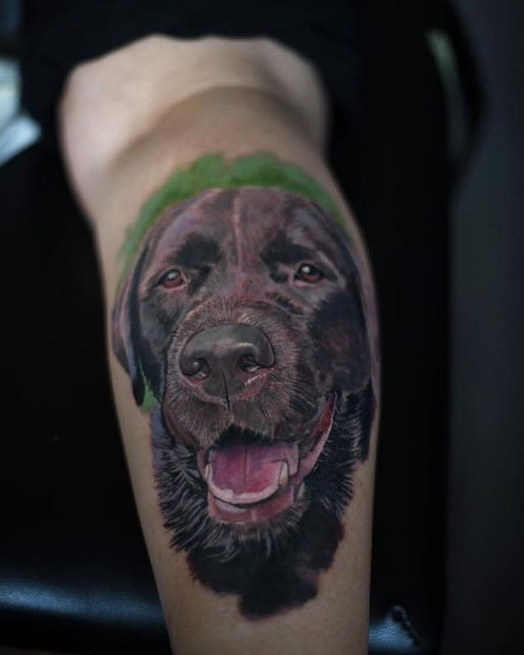 Realistisches Tattoo eines schwarzen Labradors mit detaillierter Fellstruktur und farbigen Schattierungen auf einer Wade.
